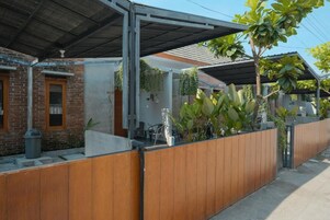 Um imóvel residencial com varanda coberta, muro de tijolos e cerca de madeira.