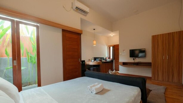 A hotel room with a bed, a desk, a television, and a sliding door to a balcony. - Andewi Guest House Denpasar (Denpasar)