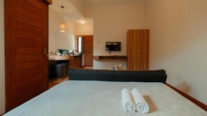 A bedroom with a bed, a TV mounted on the wall, and a wooden wardrobe. - Andewi Guest House Denpasar (Denpasar)