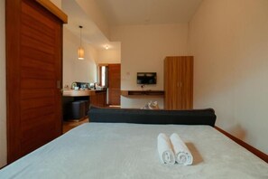A bedroom with a bed, a TV mounted on the wall, and a wooden wardrobe. - Andewi Guest House Denpasar (Denpasar)