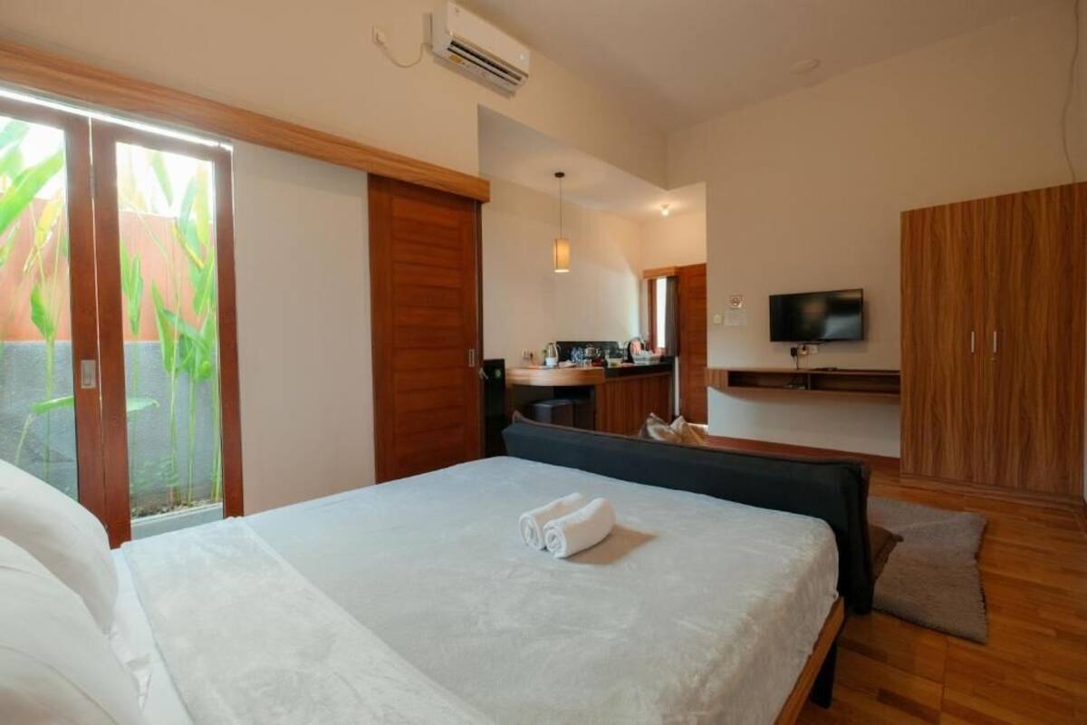 A hotel room with a bed, a desk, a television, and a sliding door to a balcony.