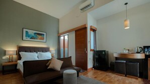 A bedroom with a bed, bedside table, and a small ottoman. There is a kitchenette with a coffee maker and a refrigerator. - Andewi Guest House Denpasar (Denpasar)
