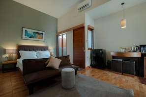 Un dormitorio con cama, mesita de noche y un pequeño reposapiés. Cuenta con una kitchenette equipada con cafetera y refrigerador.