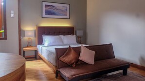 A bedroom with a bed, a brown sofa, a bedside table with a lamp, and a framed picture on the wall. - Andewi Guest House Denpasar (Denpasar)