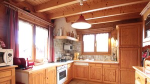 A wooden kitchen with a tiled floor, wooden cabinets, a stove, a microwave, and a hanging light fixture.