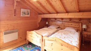 A wooden cabin bedroom with two beds, a radiator, and a painting on the wall.