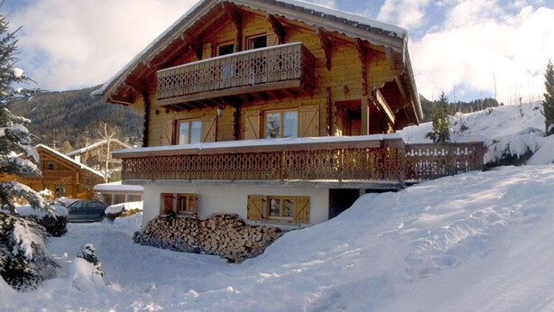 A chalet with a balcony, surrounded by snow-covered landscape and mountains.
