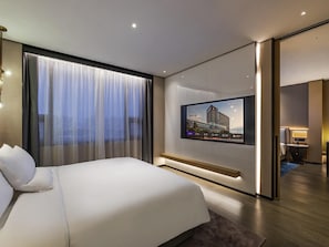 A modern hotel room with a large bed, a TV mounted on the wall, and a view of the cityscape through the window.