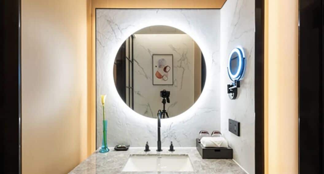 A modern bathroom with a marble sink, a circular mirror, and a ring light.
