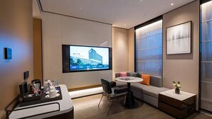 A modern hotel room with a flat-screen TV mounted on the wall, a dining area with a round table, and a seating area with a sofa and cushions. - Novotel Tianjin Drum Tower (Tianjin)