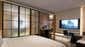 A hotel room with a bed, a desk with a chair, a television mounted on the wall, and a sliding door with frosted glass panels.