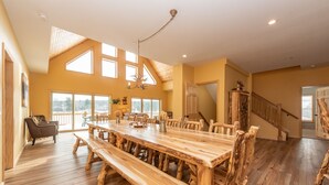 A spacious dining area with a large wooden table and benches, high ceilings with skylights, and a staircase leading to another level. - Lakefront Lodge w/ Hot Tubs, Games & More (Swanton)