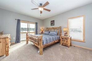A bedroom with a wooden bed, a ceiling fan, a window with blinds, and a view of the outdoors. - Lakefront Lodge w/ Hot Tubs, Games & More (Swanton)