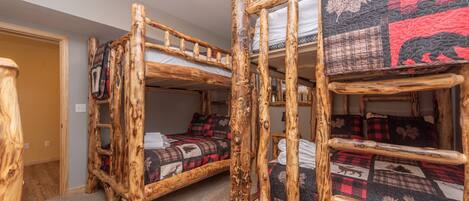 Une chambre rustique avec un lit superposé en bois, dotée d’une tête de lit matelassée et d’une échelle.