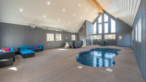 An indoor swimming pool area with a large pool, blue and red cushioned seating, and a ceiling fan. - Lakefront Lodge w/ Hot Tubs, Games & More (Swanton)