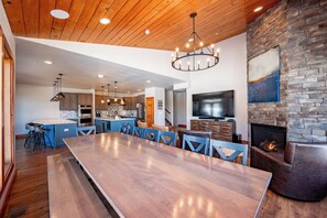 Un comedor amplio con una larga mesa de madera y sillas azules, una cocina con electrodomésticos modernos y una chimenea de piedra.