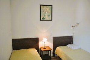 Two single beds with wooden headboards, a bedside table, and a framed painting adorn this cozy space.