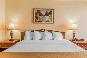 A hotel room with a bed, two bedside lamps, a painting on the wall, and a nightstand with a phone.