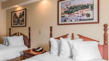 A hotel room with two beds, a wooden headboard, a bedside table with a phone, and two framed pictures on the wall.