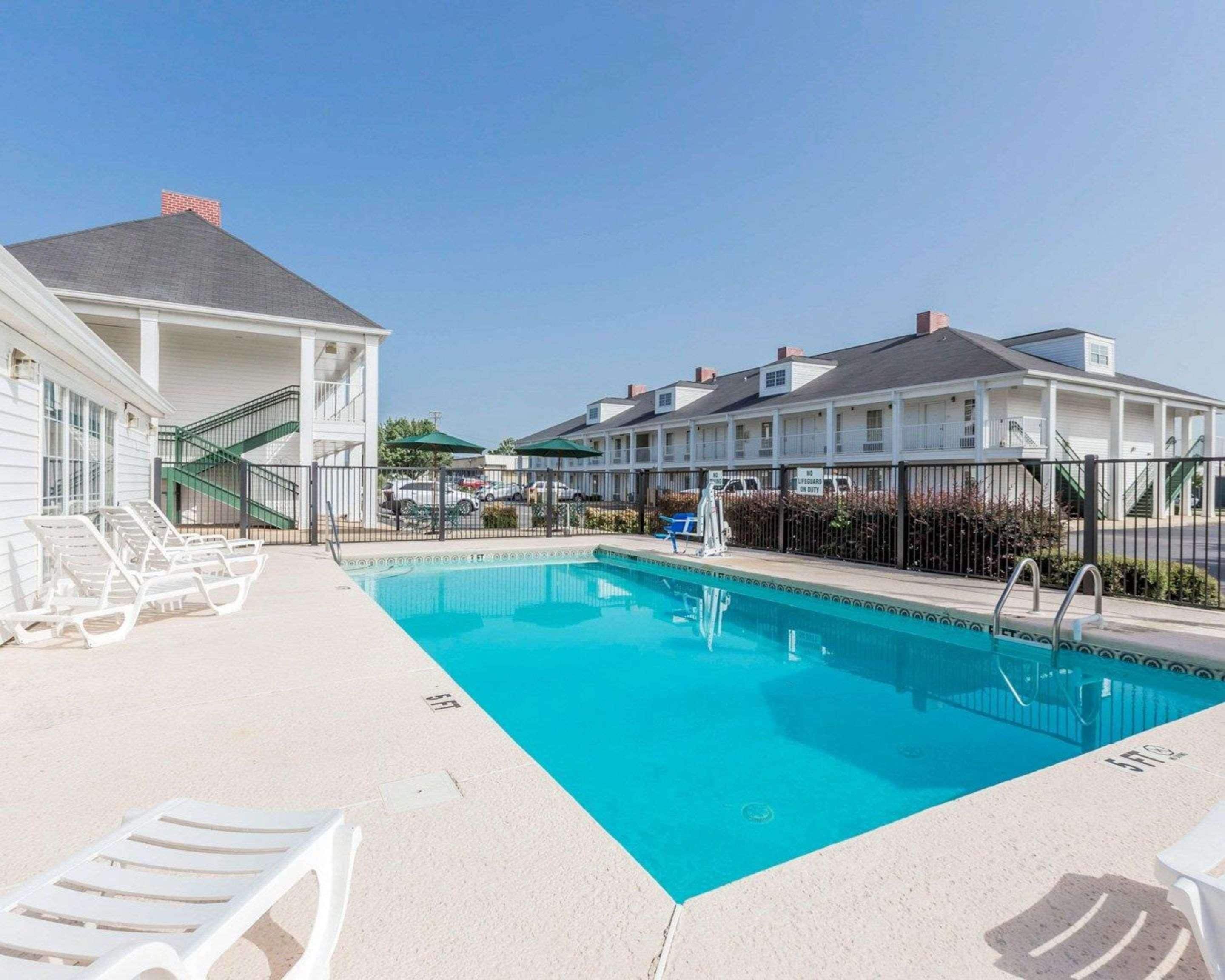 Una piscina con sillones de descanso, una escalera y un edificio con varias ventanas y balcones.