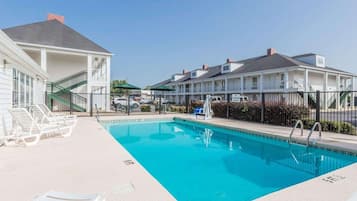 Una piscina con sillones de descanso, una escalera y un edificio con varias ventanas y balcones.