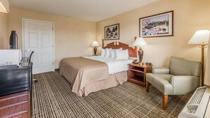 A hotel room with a bed, two bedside lamps, a chair, a desk with a computer, and a door.