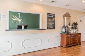 Una zona de recepción con un cartel de 'Quality Inn', un horario de registro de entrada y salida, un espejo y una estación de café.