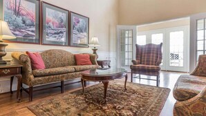 A living room with a sofa, armchair, coffee table, and a rug. There are framed pictures on the wall, a lamp, and a window with a view. - Rodeway Inn Sylacauga Hwy 280 (Sylacauga)