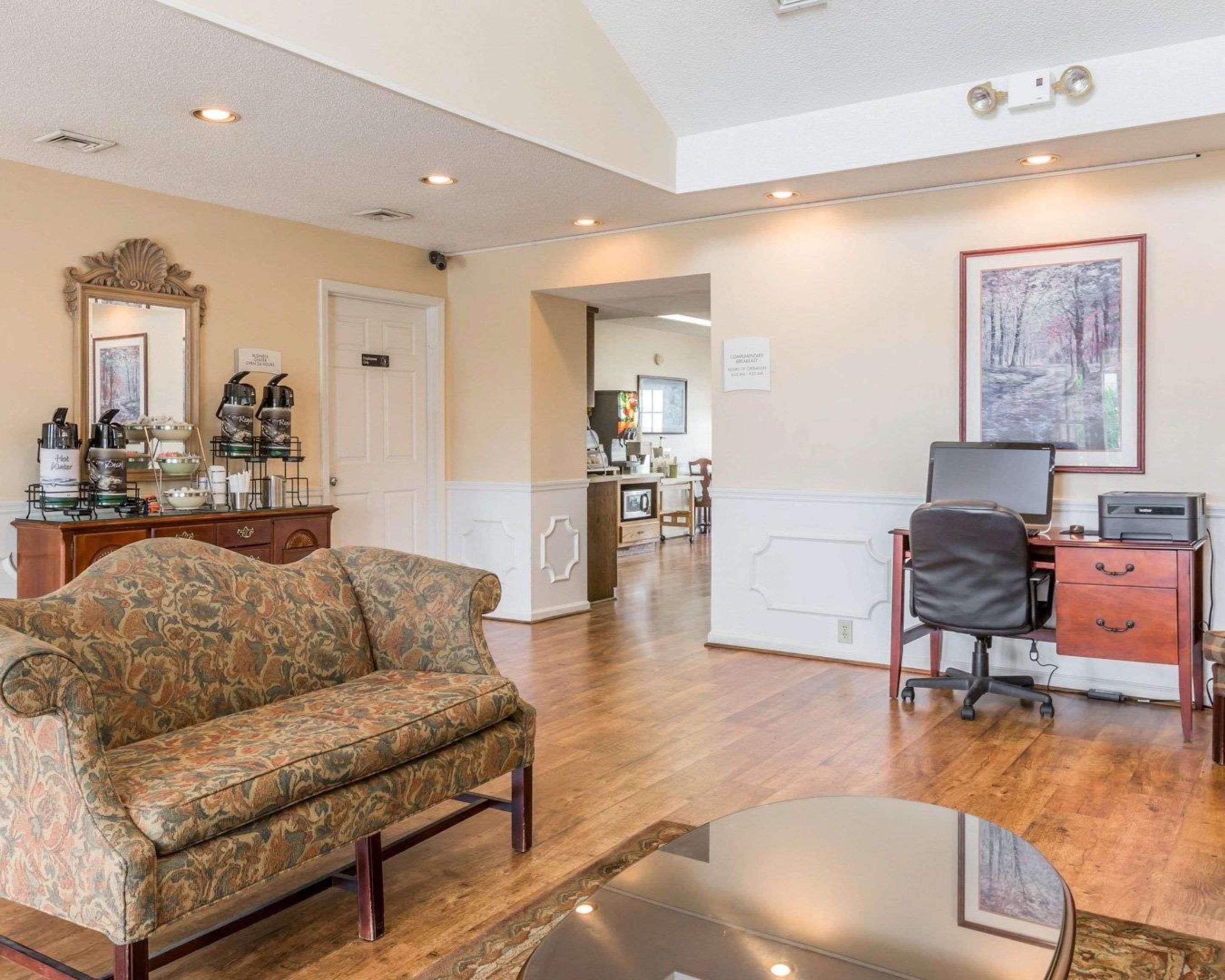A hotel room with a sofa, a desk with a computer, a coffee station, and a dining area.