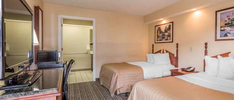 A hotel room with two beds, a desk with a computer, a chair, and a mirror.