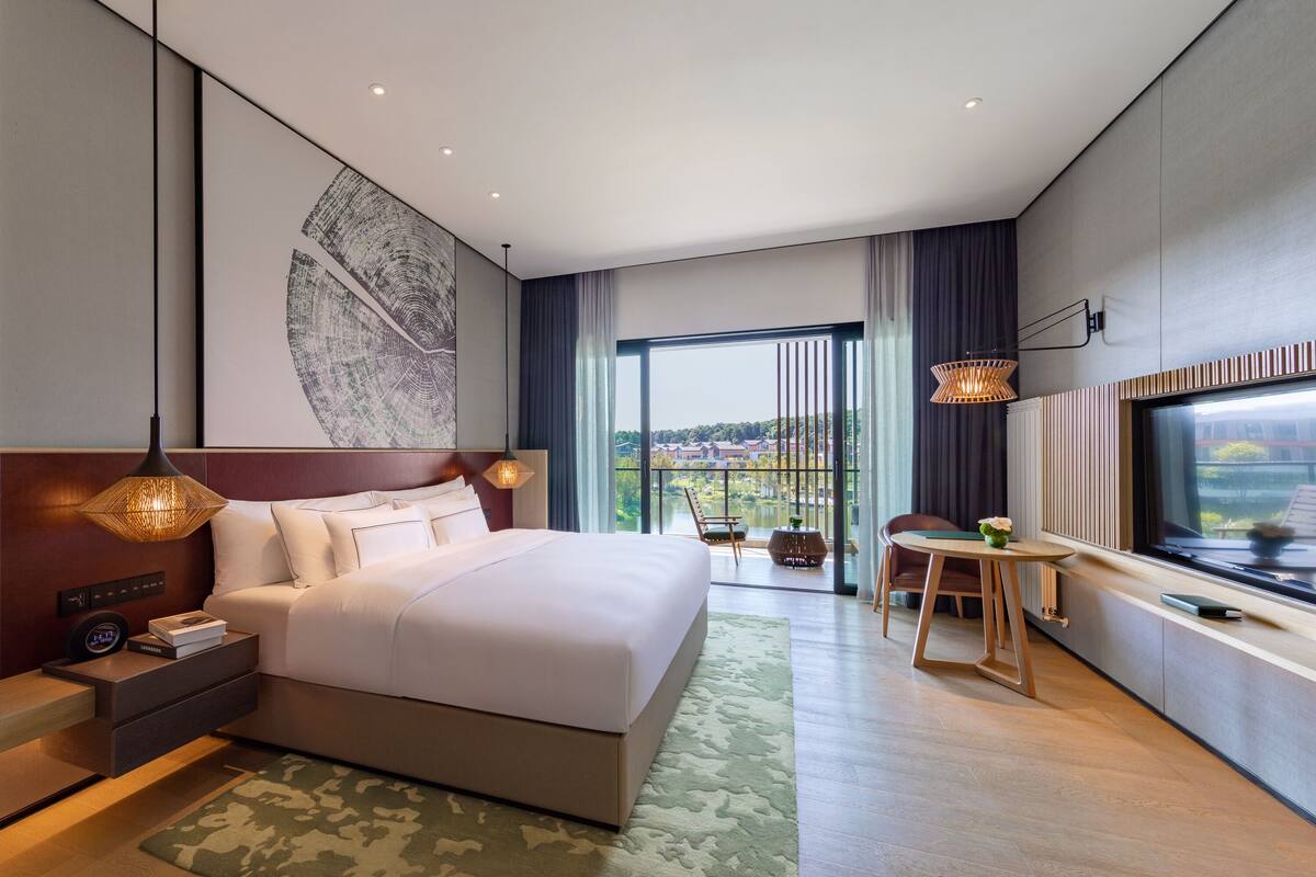A modern hotel room with a large bed, a desk, and a view of the city.