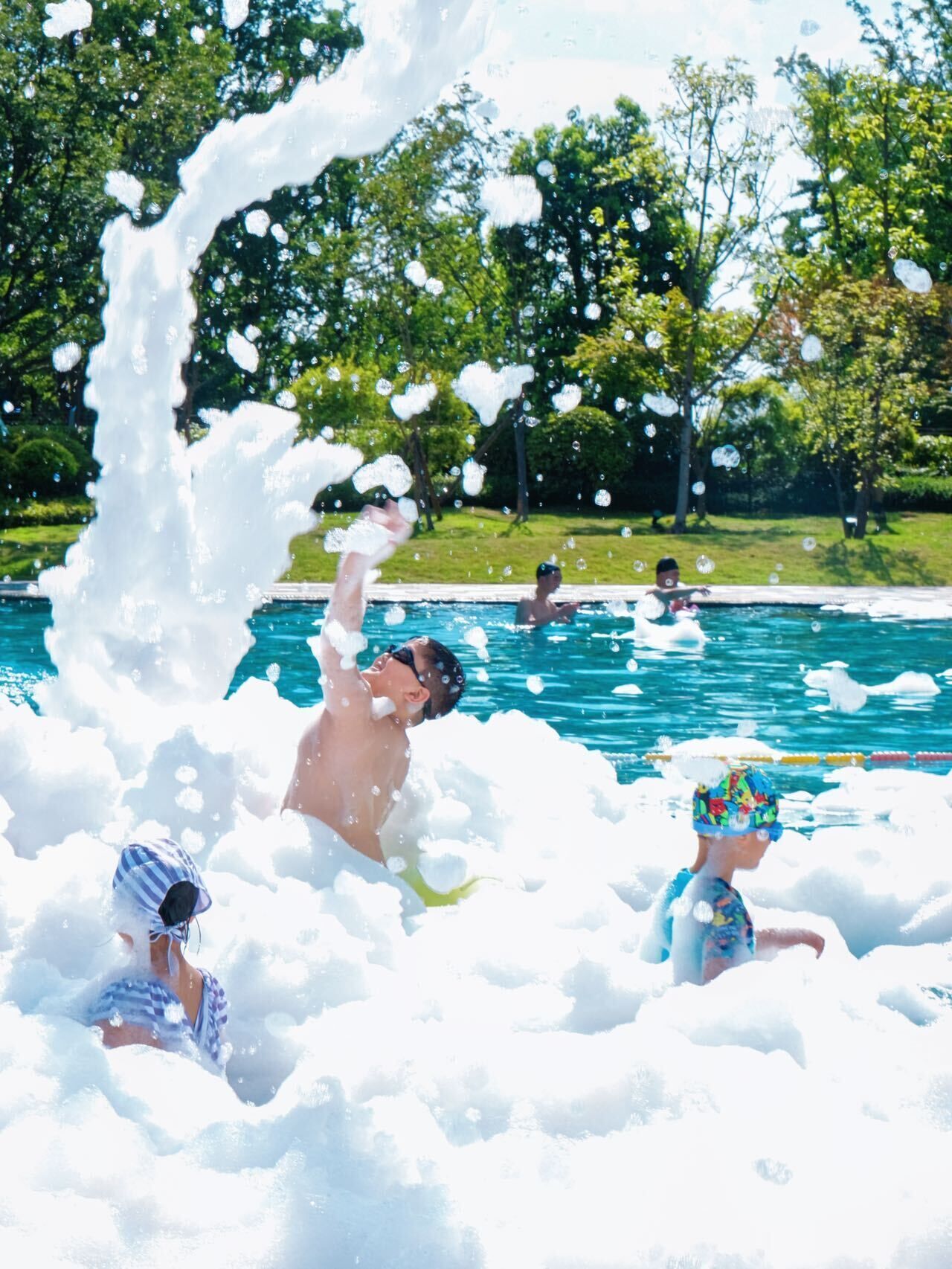 A swimming pool with people enjoying the water, surrounded by trees.