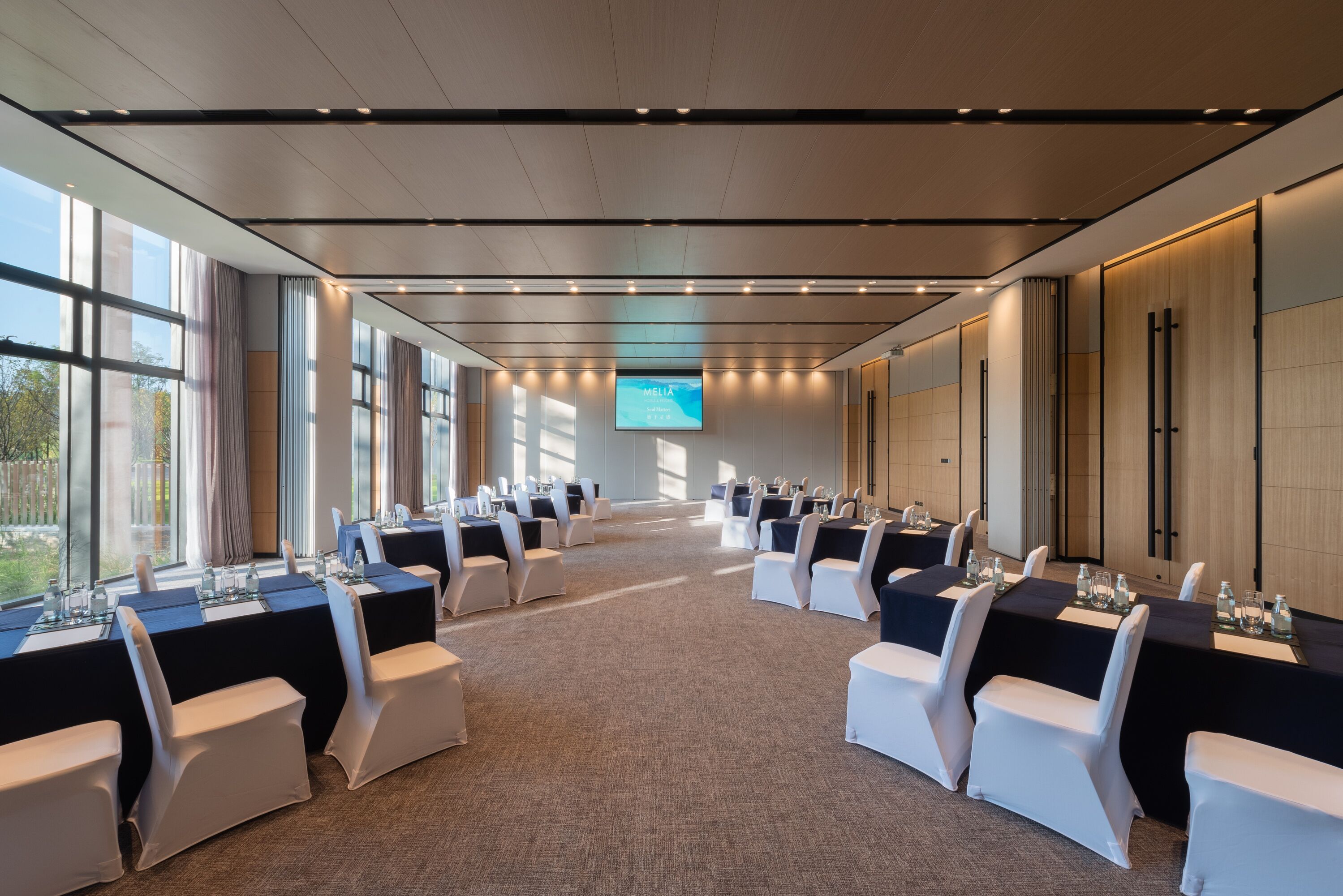 Une salle de conférence dotée de longues tables et de chaises, de grandes fenêtres et d’un écran affichant le mot « MELIA ».