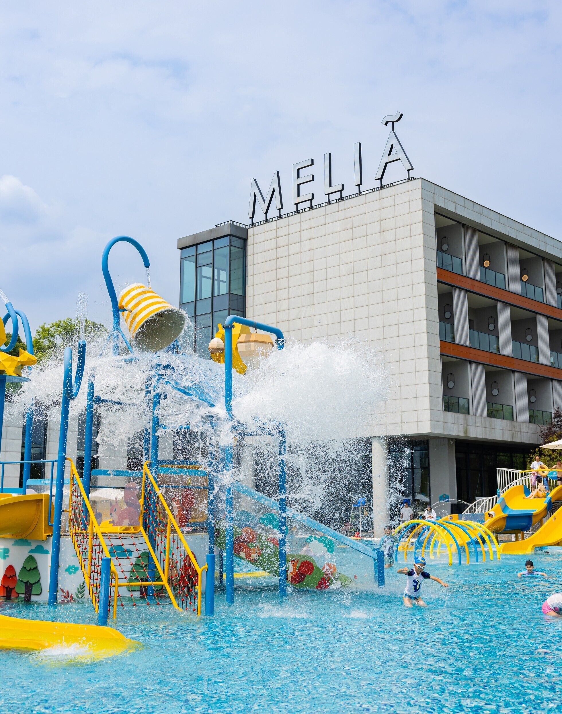 A water park with a pool, slides, and a building with 'MELIA' signage.