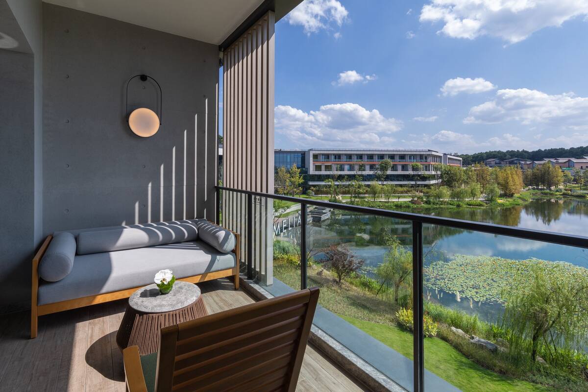 A balcony with a sofa, a small round table, and a chair. The balcony overlooks a body of water with a building in the background.
