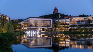 A modern hotel with a large reflective pool, a pagoda in the background, and the name 'MELIA' illuminated on the building facade. - Melia Chongqing (Chongqing)