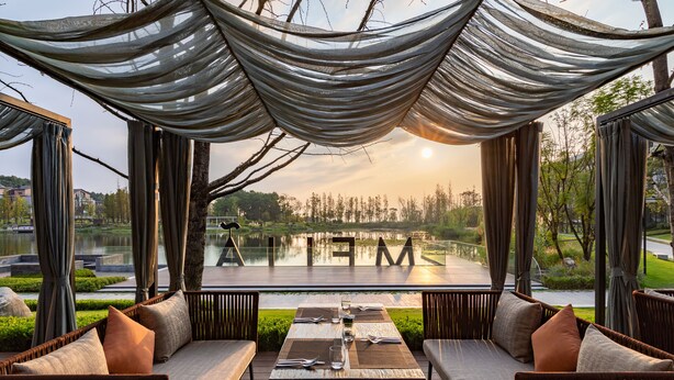 An outdoor seating area with a view of a lake and trees, featuring a table set for dining. - Melia Chongqing (Chongqing)