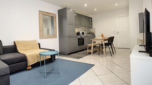Un apartamento moderno con un sofá gris, una alfombra azul, una cocina con armarios grises y un comedor con una mesa y sillas.