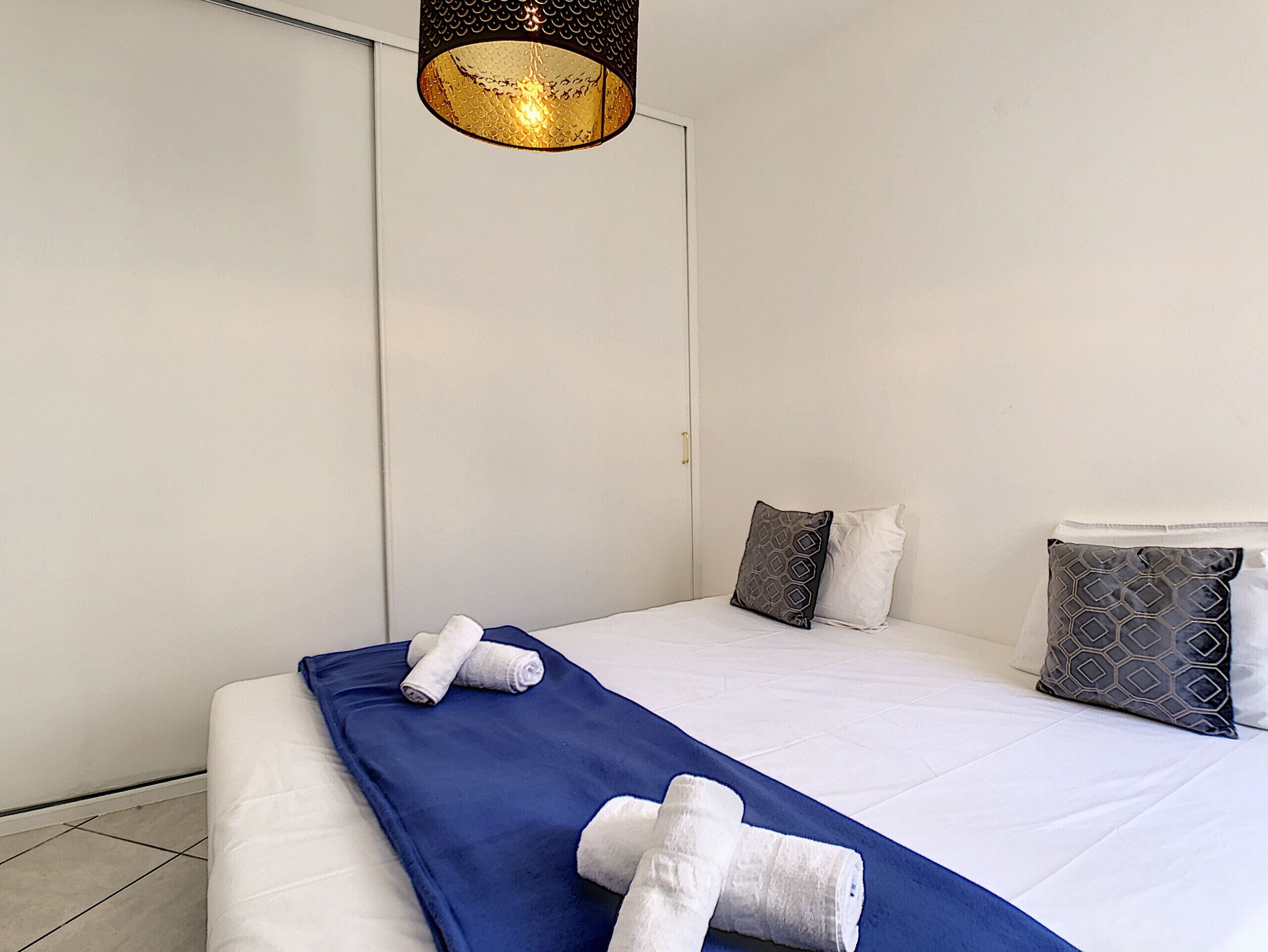 Una habitación de hotel con una cama grande, ropa de cama blanca, un edredón azul y dos toallas enrolladas.