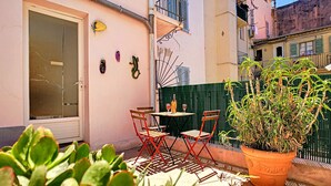 Un pequeño patio al aire libre con una mesa, sillas, una planta en maceta y una puerta con ventanal.