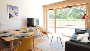 A modern living room with a dining area, a television, and a large window with a view of trees.