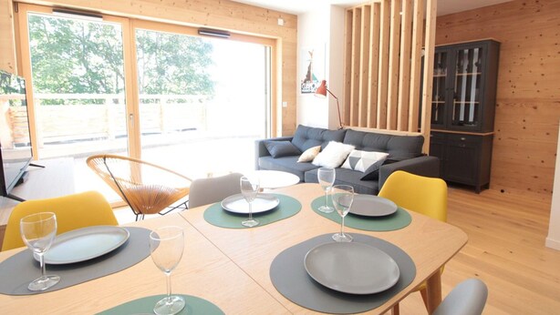 A modern living room with a dining area, featuring a wooden floor, a sofa, a cabinet, and a dining table set for four.