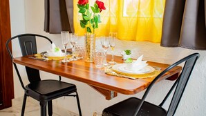 Una mesa de comedor servida con platos blancos, vasos transparentes y un florero con rosas rojas.