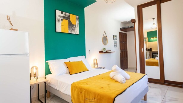 Un dormitorio moderno con cama, mesita de noche, cuadro abstracto en la pared, espejo y puerta que da al baño.