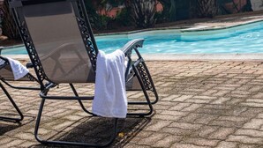 Una silla de descanso junto a la piscina, con una toalla blanca, una piscina y un patio de ladrillo.
