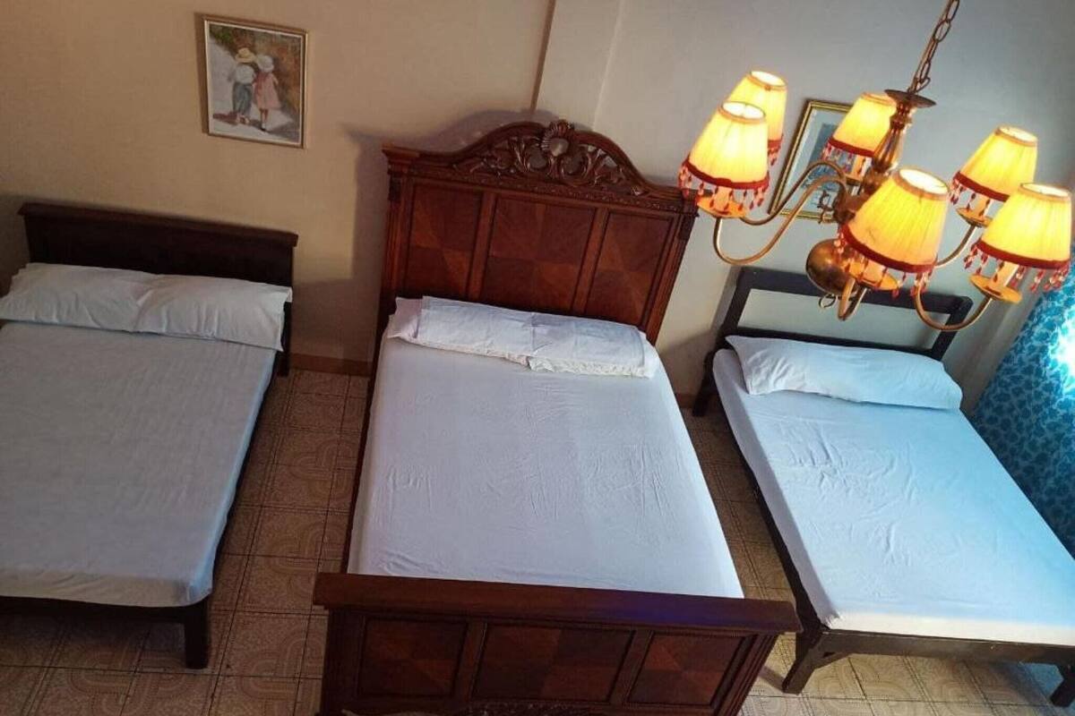 A room with three single beds, a wooden headboard, a painting on the wall, and a chandelier.