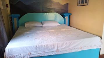 Un letto con una coperta bianca e azzurra, due cuscini e un murale raffigurante un paesaggio montano.