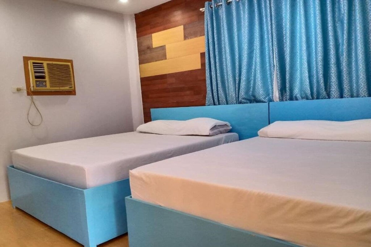 A room with two beds, a wooden headboard, a wall-mounted air conditioner, and blue curtains.