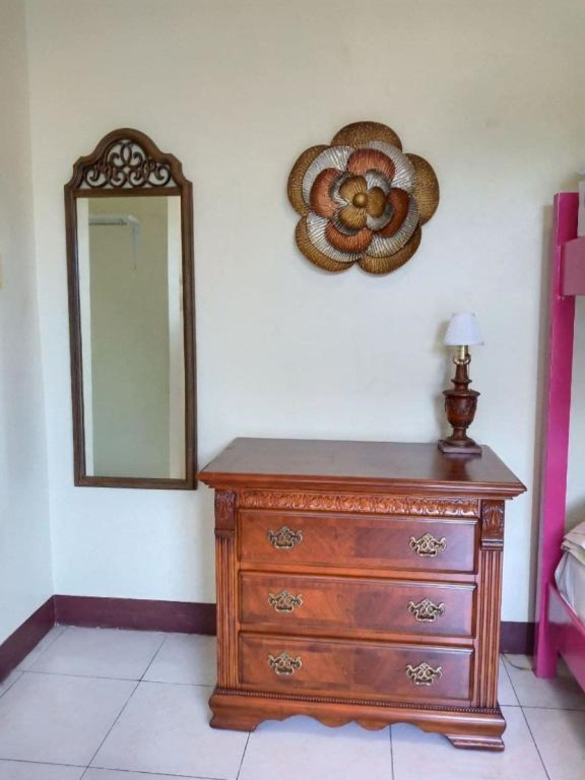 A wooden dresser with drawers and a mirror above it, a decorative wall piece, and a lamp on top of the dresser.