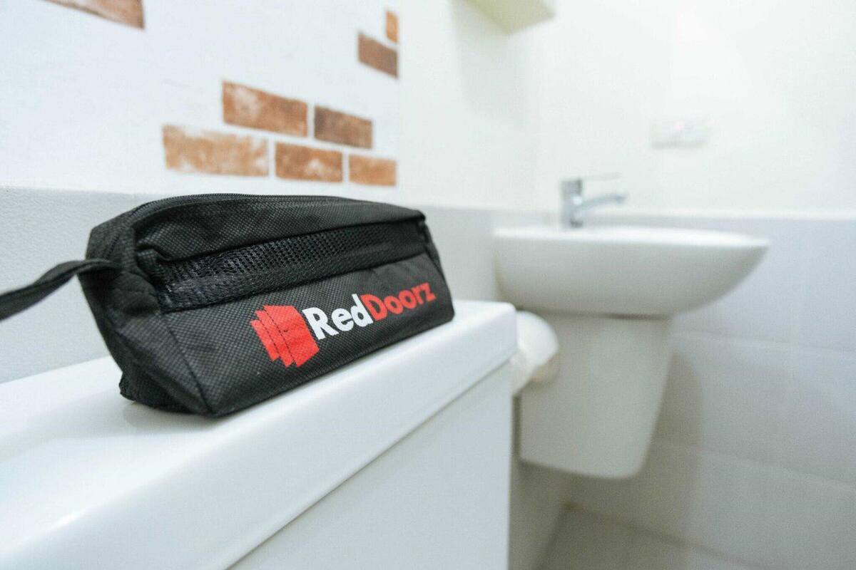 A black bag with "RedDoorz" on a white toilet in a bathroom with a white sink and brown tiles.